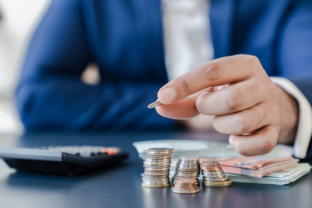 Businessman holding euro cents coins dollar bills on table with pile of coins and banks calculator, managing dividing money to save and invest it to make income. Saving money and investing concept.