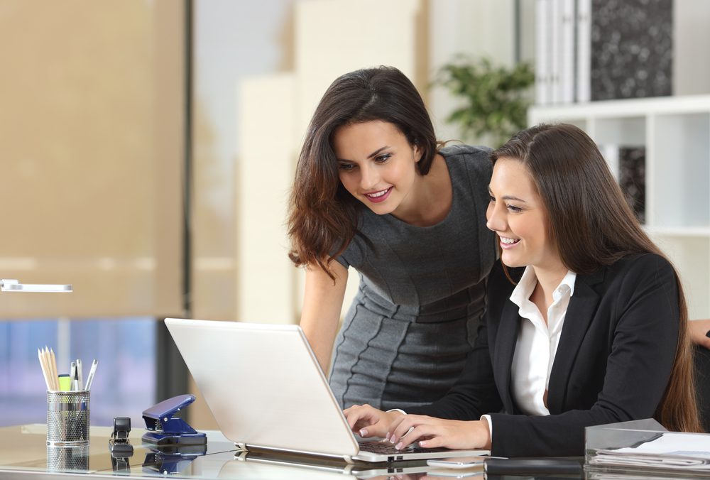 Two happy businesswomen coworking with a laptop in a desktop at office